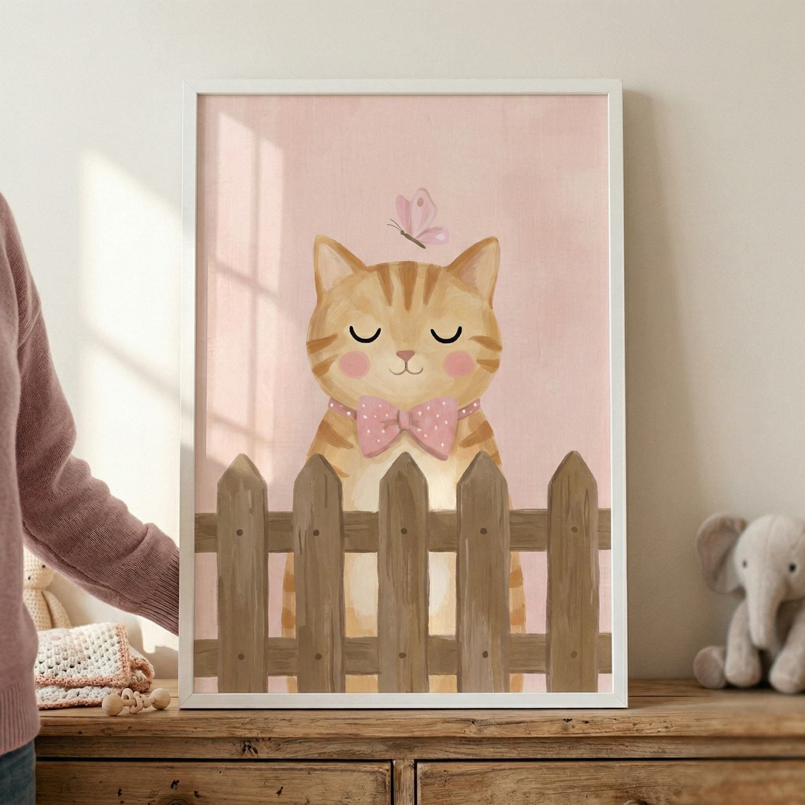 A framed piece of wall art featuring a whimsical illustration of an orange striped kitten. The kitten has a peaceful expression with its eyes closed and soft pink circles on its cheeks. It wears a charming pink bow tie with white polka dots. A small, light pink butterfly floats gracefully just above the kitten's head.

