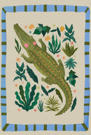 Close up of a playful crocodile illustration with green scales, pink cheeks, and small orange star details surrounded by leafy plants on a soft neutral background. The whimsical jungle design highlights the texture and colors of the artwork for nursery wall decor.