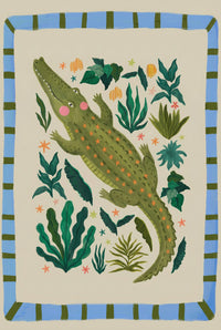 Close up of a playful crocodile illustration with green scales, pink cheeks, and small orange star details surrounded by leafy plants on a soft neutral background. The whimsical jungle design highlights the texture and colors of the artwork for nursery wall decor.