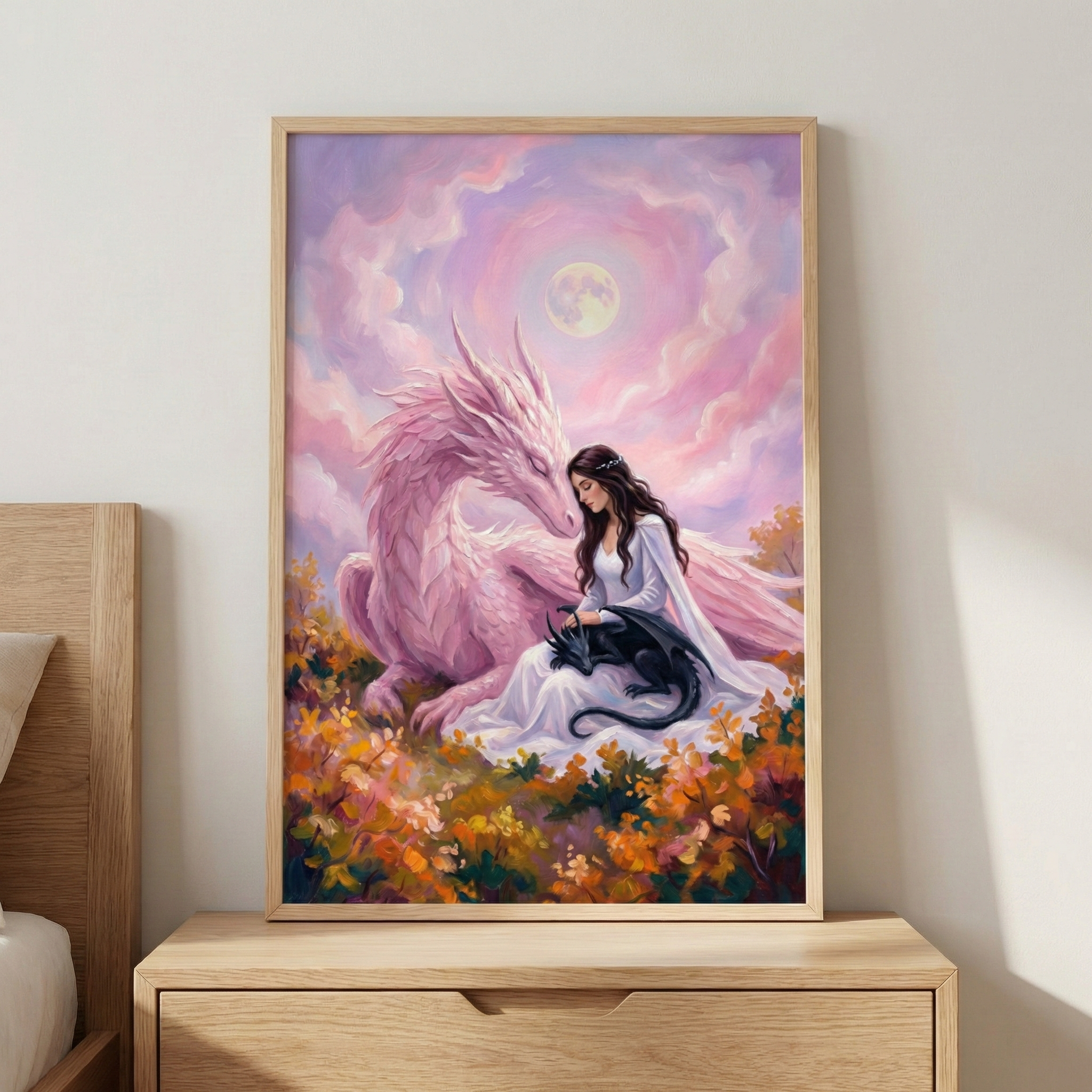 A framed fantasy illustration depicts a woman in a flowing white dress sitting peacefully in a field of colorful autumn leaves. Beside her, a large, pale pink dragon rests its head near her shoulder. In her lap, a small black dragon curls up asleep. The scene is set against a whimsical background of swirling pink and purple clouds under a bright full moon, creating a serene and magical atmosphere.