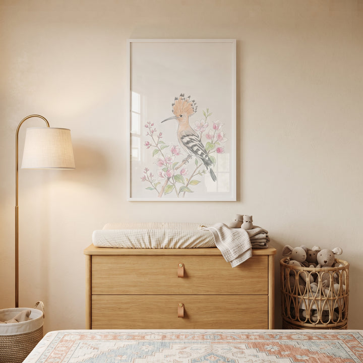Pink floral crested hoopoe wall art above a wooden dresser in a neutral nursery with a lamp and toy basket.