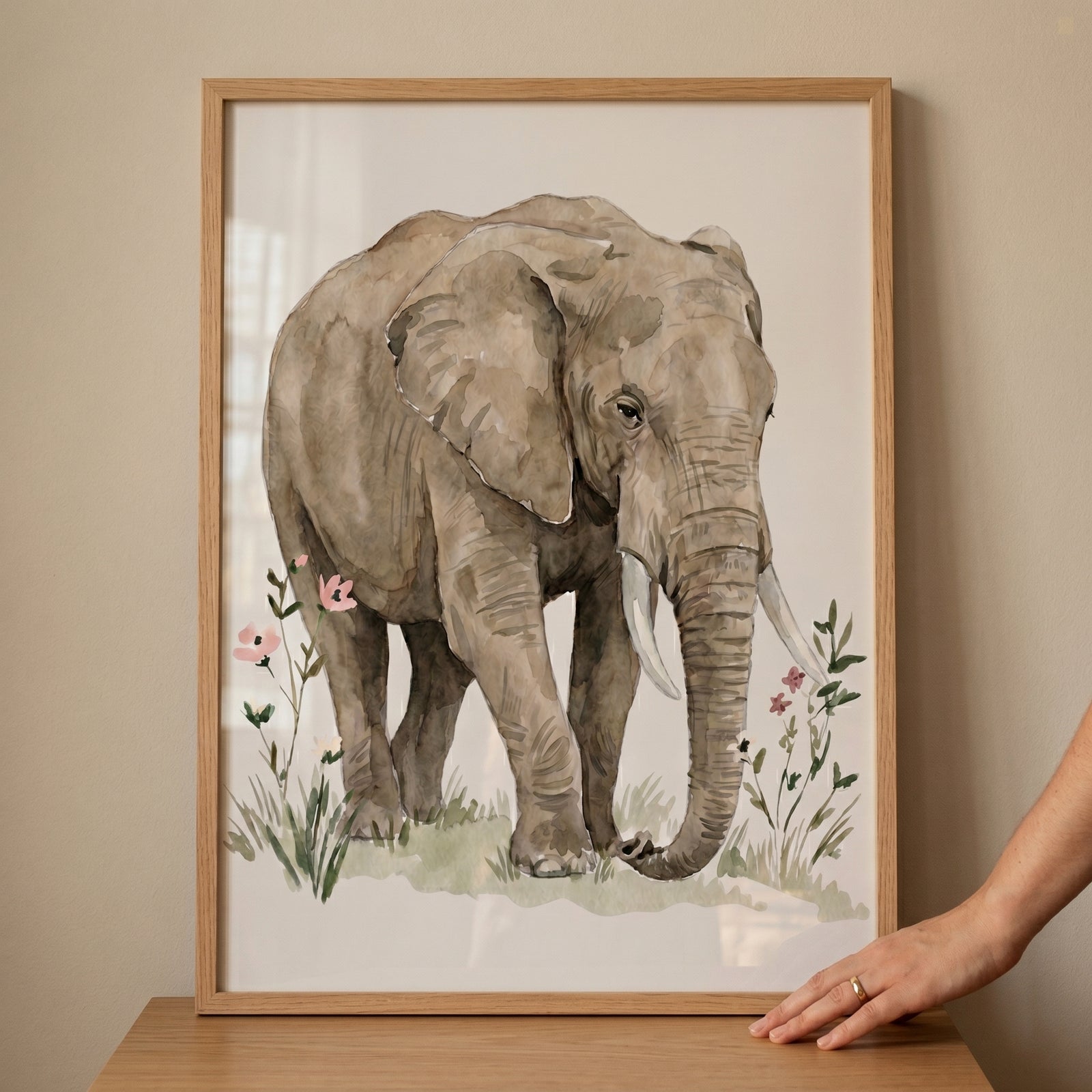 Framed pink flower elephant wall art features a brown elephant walking through green grass and small pink flowers.