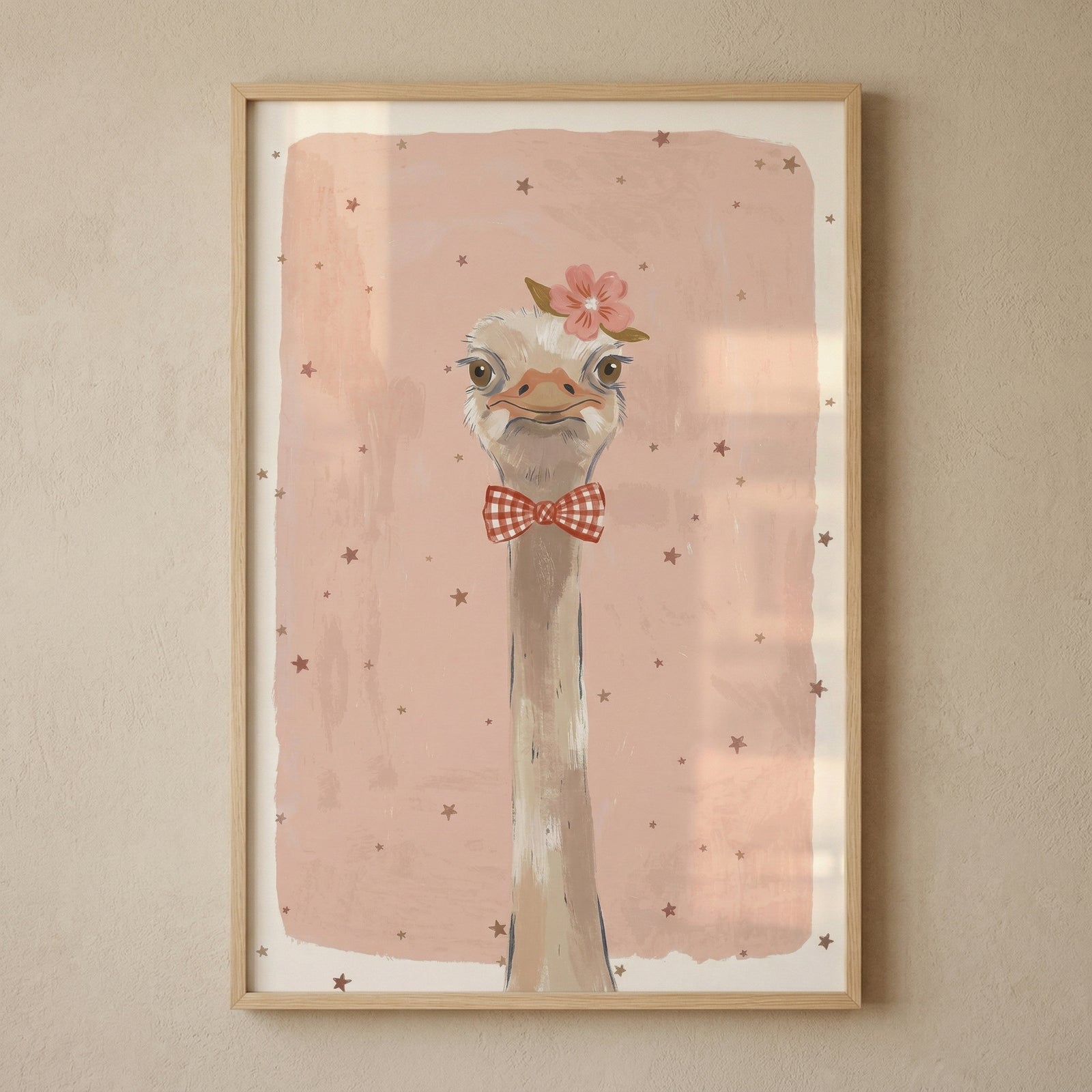 Framed illustration of an ostrich with a long neck wearing a red checkered bow tie and a pink flower on its head against a soft pink background with scattered stars. The playful portrait style artwork adds a lighthearted and whimsical touch to a nursery or child’s room wall.
