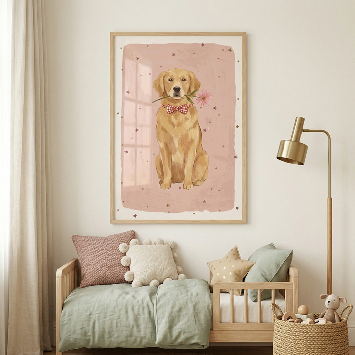 A framed illustration of a golden retriever hangs on a light-colored wall in a serene nursery setting. The dog is depicted wearing a red-and-white checkered bow tie and holding a single pink flower in its mouth against a soft pink backdrop with small star shapes. Below the artwork, a wooden daybed is styled with a sage green duvet and several decorative pillows in shades of pink, cream, and green. A sleek gold floor lamp and a woven basket of toys complete the warm, neutral room.