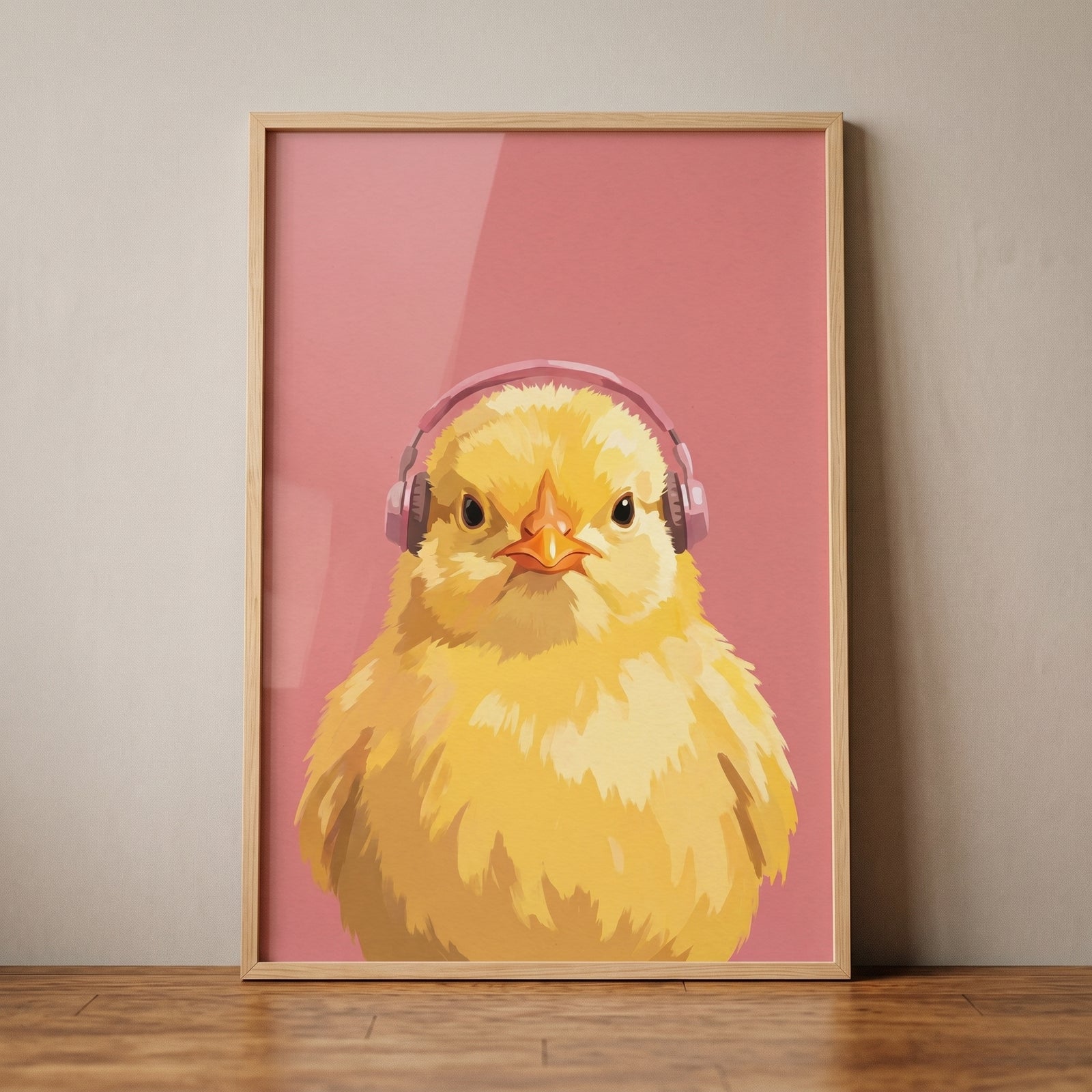 Pink headphones yellow chick wall art in a wooden frame rests on a floor against a neutral wall.