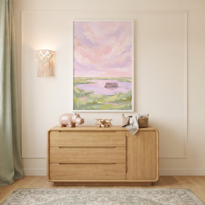 Pink pastel sky hippo animal wall art hangs above a wooden dresser with a toy hippo and airplane in a nursery.