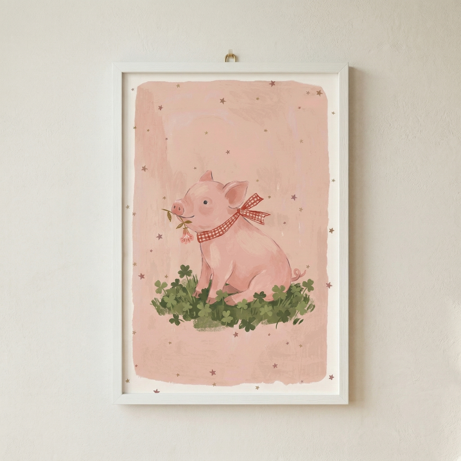 A whimsical illustration of a small, pink pig sitting on a bed of green clovers. The pig is shown with a gentle expression, holding a tiny sprig with a pink flower in its mouth. Around its neck is tied a red and white checkered ribbon. The backdrop is a soft pink, punctuated by small, brown star-like shapes. This artwork is housed in a clean white frame and hung on a neutral, textured wall.