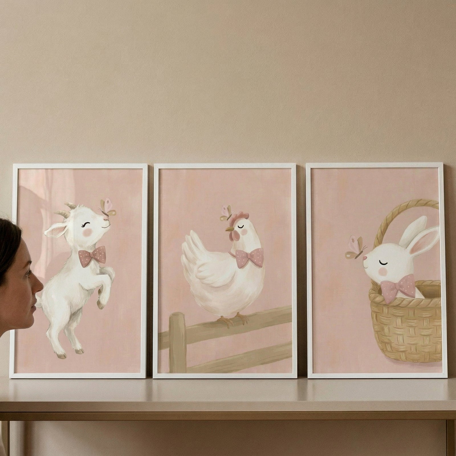 A set of three vertical nursery art prints in thin white frames, arranged in a row. The art has a soft, whimsical watercolor style with a gentle, textured blush pink background.

The first print on the left features a cute white baby goat with a tiny gold crown and a dusty pink bow tie, leaping gently towards a small butterfly.
