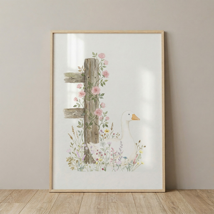A vertical, rectangular piece of watercolor art in a light wood frame leans against a neutral-colored wall on a wooden floor. The artwork features a serene scene on a white background. On the left, a weathered wooden fence post is adorned with climbing pink roses and green leaves. To the right of the post, a white goose with an orange beak sits peacefully among a cluster of delicate wildflowers in soft shades of pink, purple, yellow, and blue.