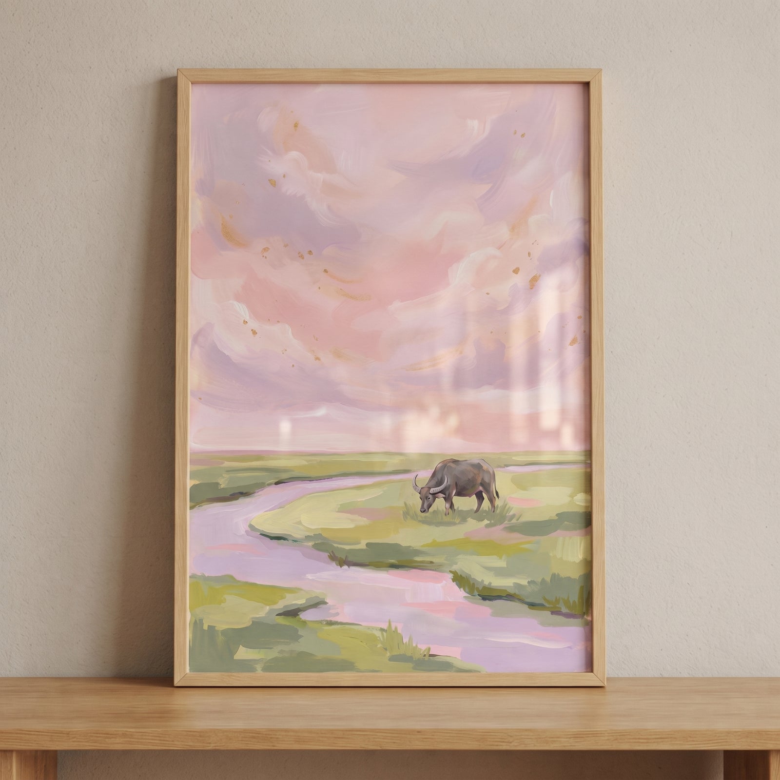 Pink sky grazing buffalo animal wall art in a wooden frame shows a buffalo by a winding river under pastel clouds.
