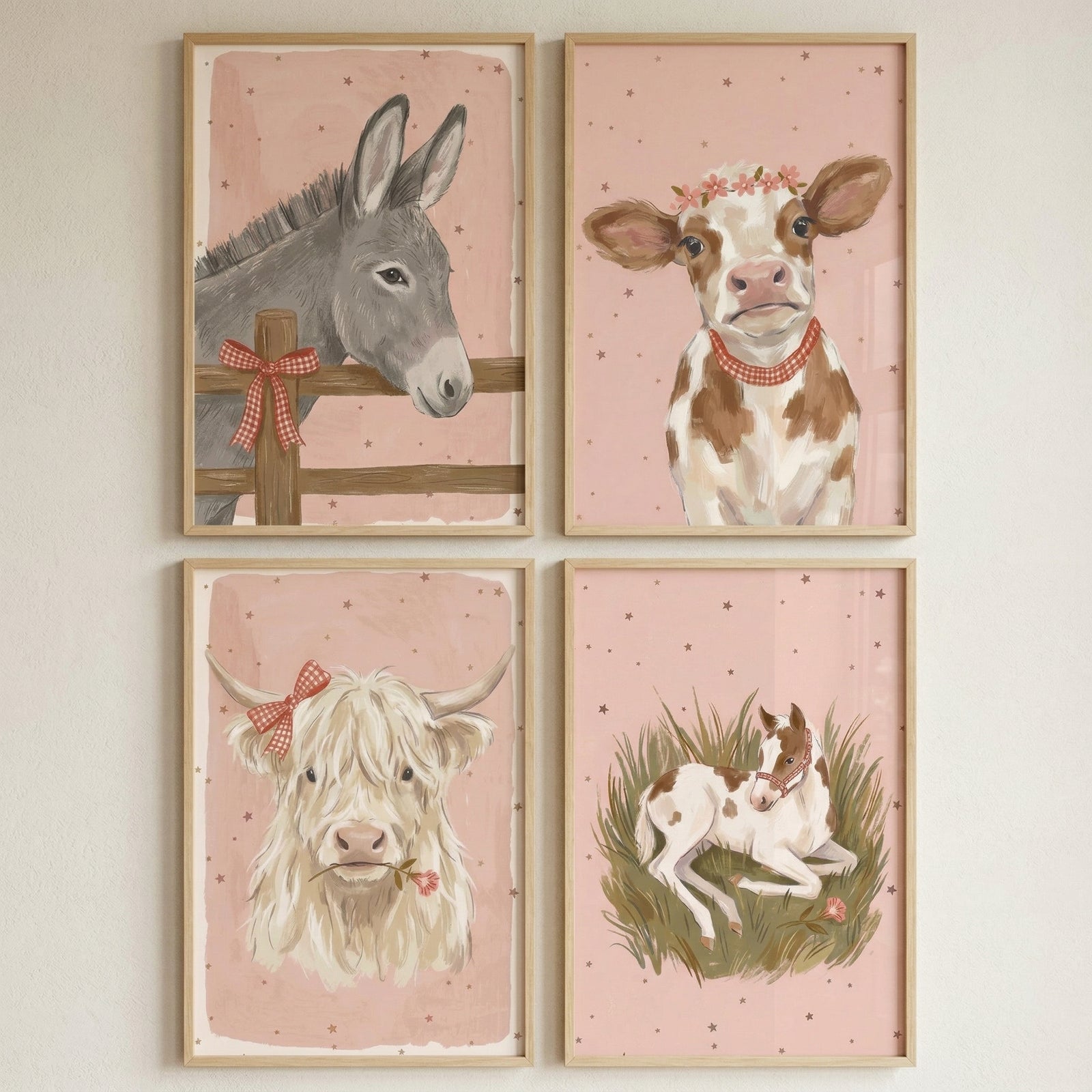 Four framed illustrations of farm animals are arranged in a square on a plain wall. Each piece features a soft pink background with delicate speckles. The top-left depicts a grey donkey behind a wooden fence adorned with a red checkered bow. To its right is a brown and white calf wearing a crown of flowers and a red necklace. Below, a fluffy white cow with horns sports a red checkered bow and holds a pink flower. The final image shows a small brown and white horse resting in tall grass.