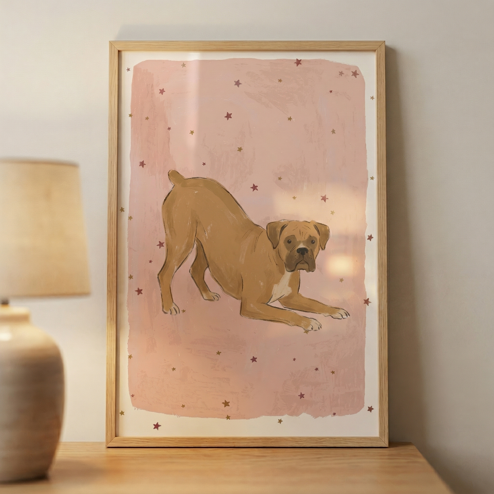 A vertical framed artwork featuring an illustration of a tan dog in a playful bowing position. The dog, which has a short muzzle and ears that fold forward, is captured with its front legs extended on the ground and its hind legs standing. This central figure is placed against a soft, textured pink background that has a slightly distressed appearance. 