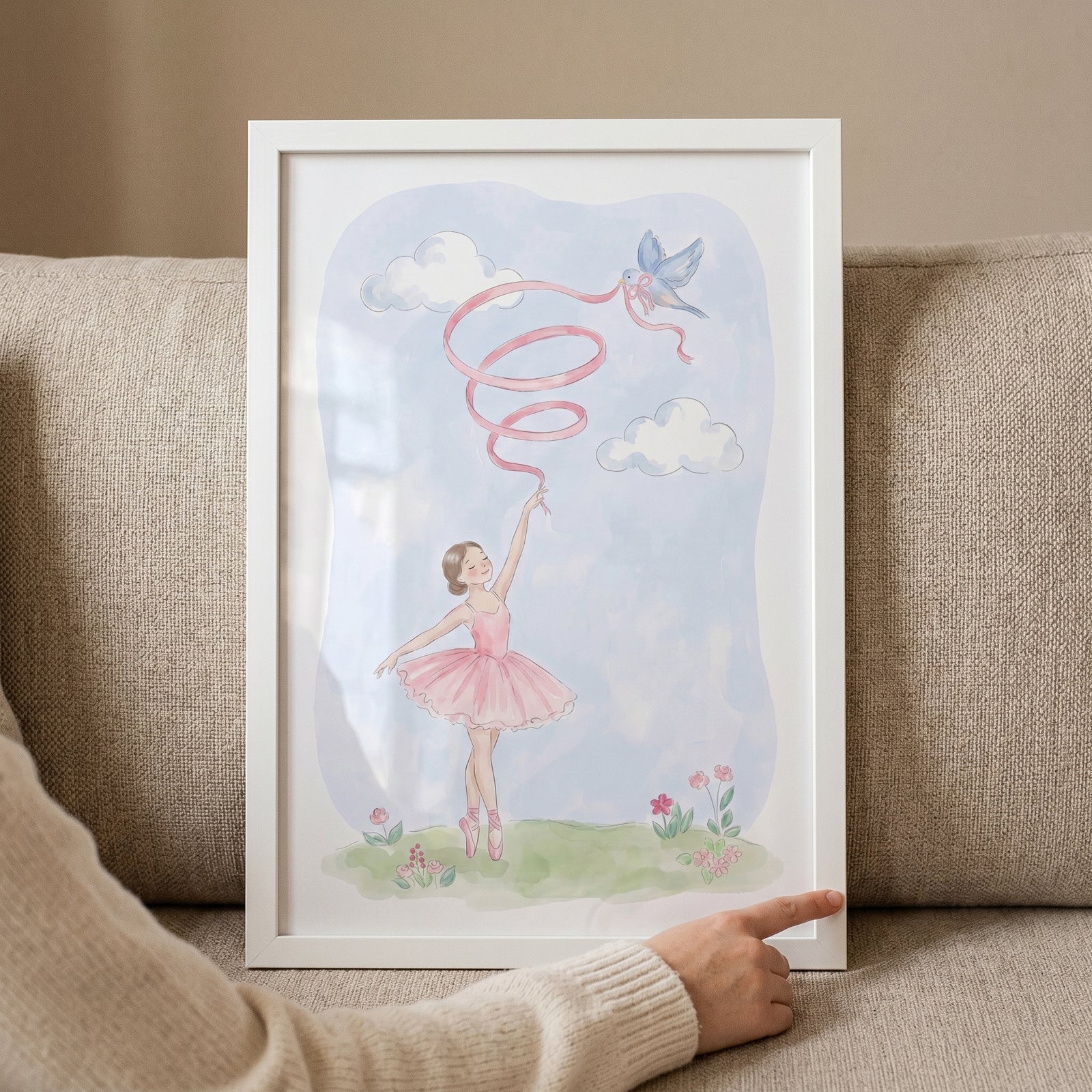 Framed pink tutu ballerina wall art shows a girl with a ribbon and a bird in the sky, held against a couch.