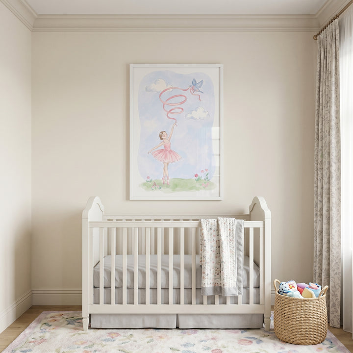 White crib sits beneath pink tutu ballerina wall art in a neutral nursery with a floral rug and woven toy basket.