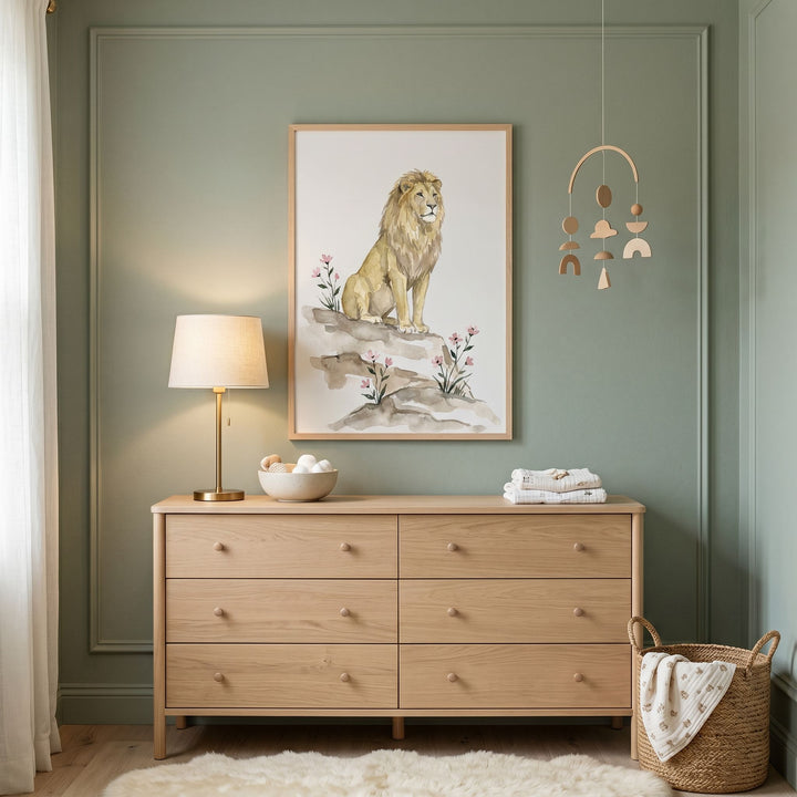 Framed pink wildflower lion wall art hangs above a light wood dresser in a green room with a lamp and mobile.