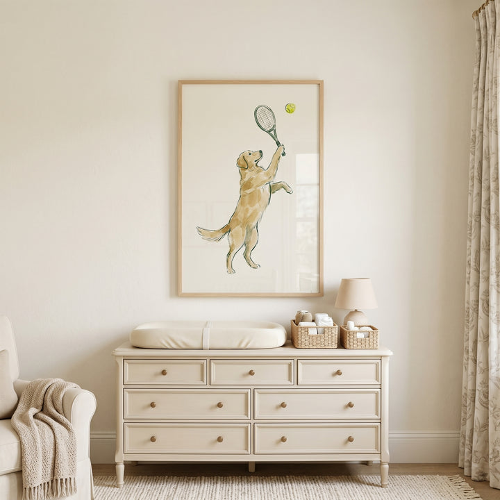 Playing tennis golden retriever wall art hangs above a cream dresser with a changing pad in a neutral room.