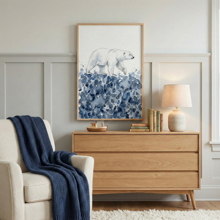 Polar bear watercolor artwork hanging above a light wood dresser in a softly lit room, with cool blue brushstrokes evoking a winter landscape. The scene is styled with neutral decor and a cozy reading nook, enhancing the animal’s serene presence.
