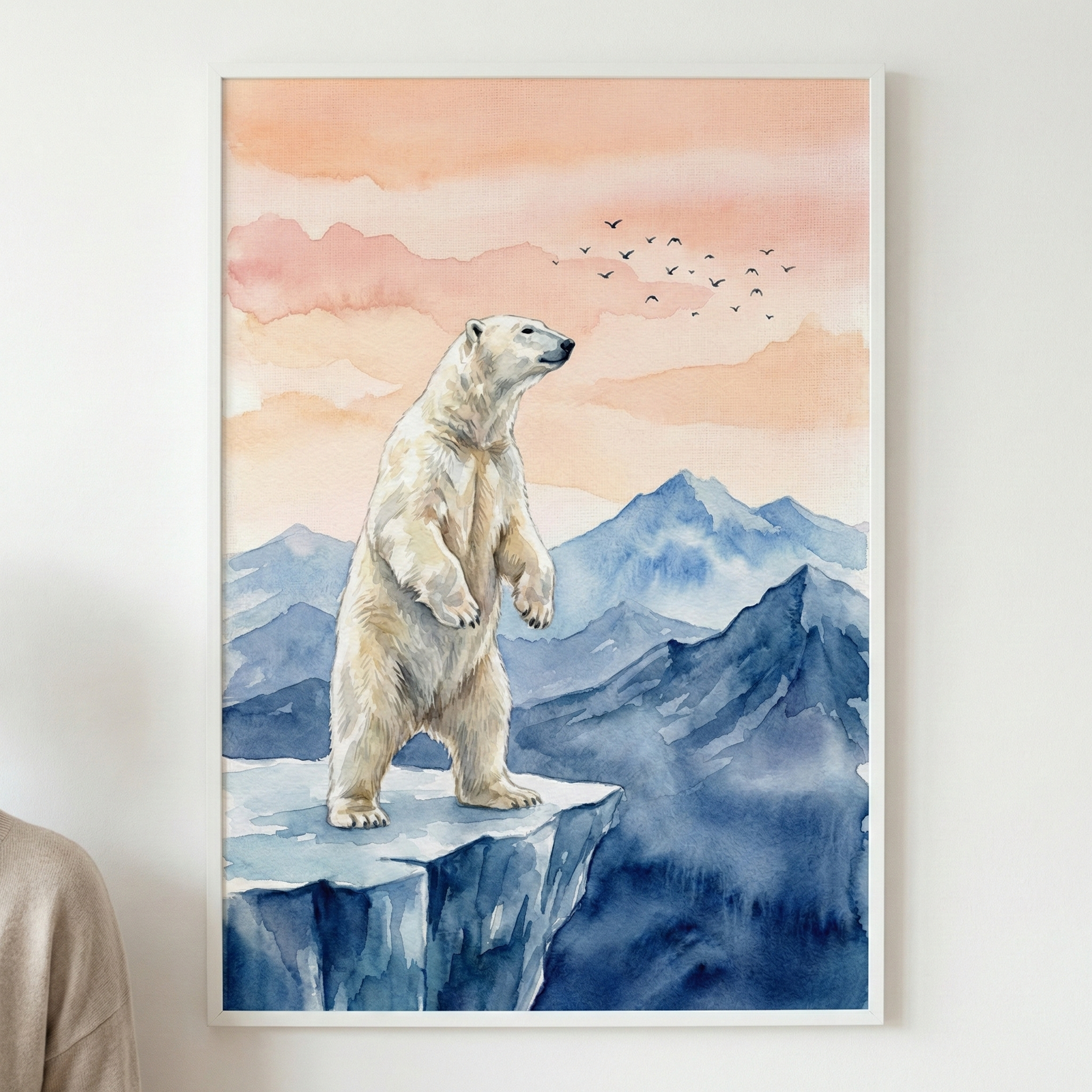 A vertical watercolor illustration depicts a polar bear standing on its hind legs atop a blue-toned cliff. The bear looks toward the right side of the frame across a series of rugged mountain ranges rendered in shades of indigo and slate. The sky is a gradient of peach, soft pink, and orange, with a scattered flock of small birds flying in the distance. The artwork uses fluid washes and textured strokes to create a serene arctic scene, displayed in a simple white frame.
