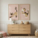 A cozy and stylishly decorated room, likely a nursery or child's bedroom, features two large, vertically oriented, wood-framed illustrations on a light-colored wall with classic paneling. 

The illustration on the left displays a stylized tan-colored cat with darker markings, shown in a deep stretch. The cat wears a small pink bow around its neck, and a tiny pink butterfly floats near its raised tail. The background is a soft, muted pink.