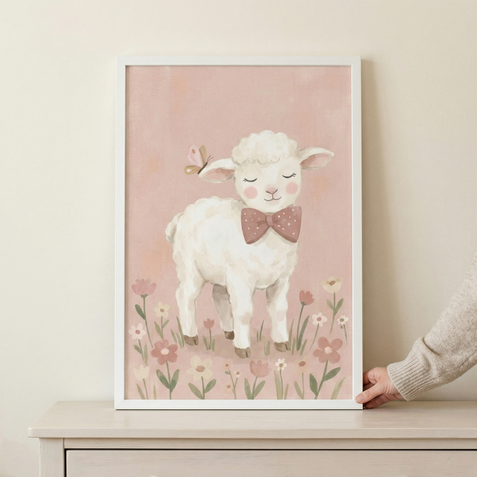 A framed nursery wall art print featuring a gentle illustration of a fluffy white lamb. The lamb has a sweet, peaceful expression with closed eyes, rosy pink cheeks, and a small pink butterfly perched on its ear. It is wearing a charming mauve bow tie with white polka dots. The lamb stands among a cluster of simple wildflowers in shades of pink and yellow. 
