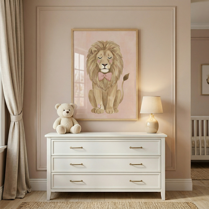 A nursery interior features a white three-drawer dresser with gold-colored handles centered against a muted pink wall with decorative molding. On top of the dresser sits a soft, beige plush toy bear on the left and a small, illuminated table lamp with a neutral-toned base and shade on the right. Hanging above the dresser is a framed illustration of a stylized lion with a pink bow tie and its eyes closed, set against a soft pink backdrop. 