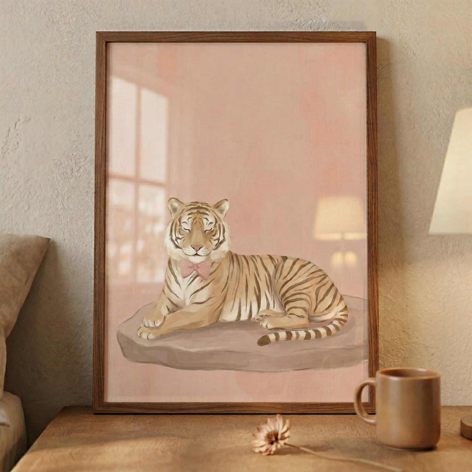 A framed digital illustration features a serene tiger resting on a flat, grey stone. The tiger is rendered in warm tan and orange tones with distinct dark stripes and wears a small, charming pink bow tie around its neck. Its eyes are gently closed in a peaceful expression. The background of the artwork is a soft, muted peach color. 
