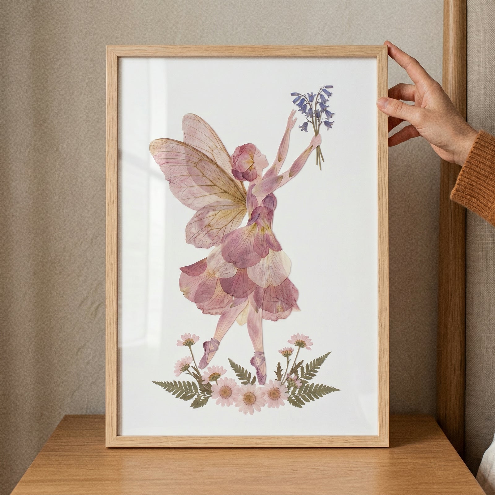 Framed pressed flower pink fairy wall art featuring a winged floral figure holding blue flowers above pink daisies.