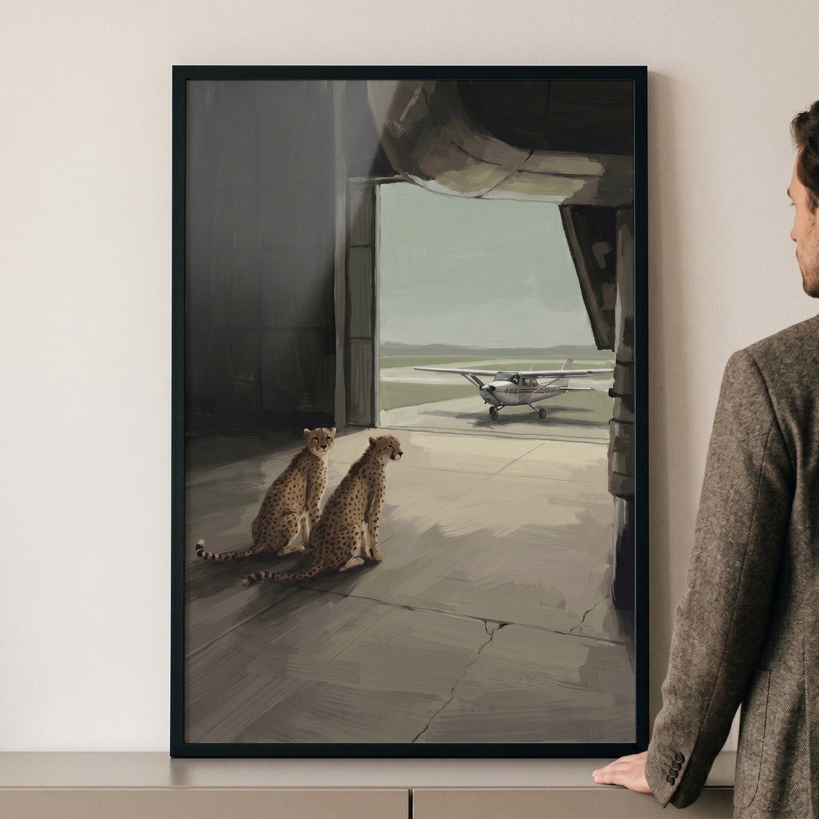 Man next to framed propeller plane watching cheetah artwork showing two cheetahs in a hangar looking at a small aircraft.