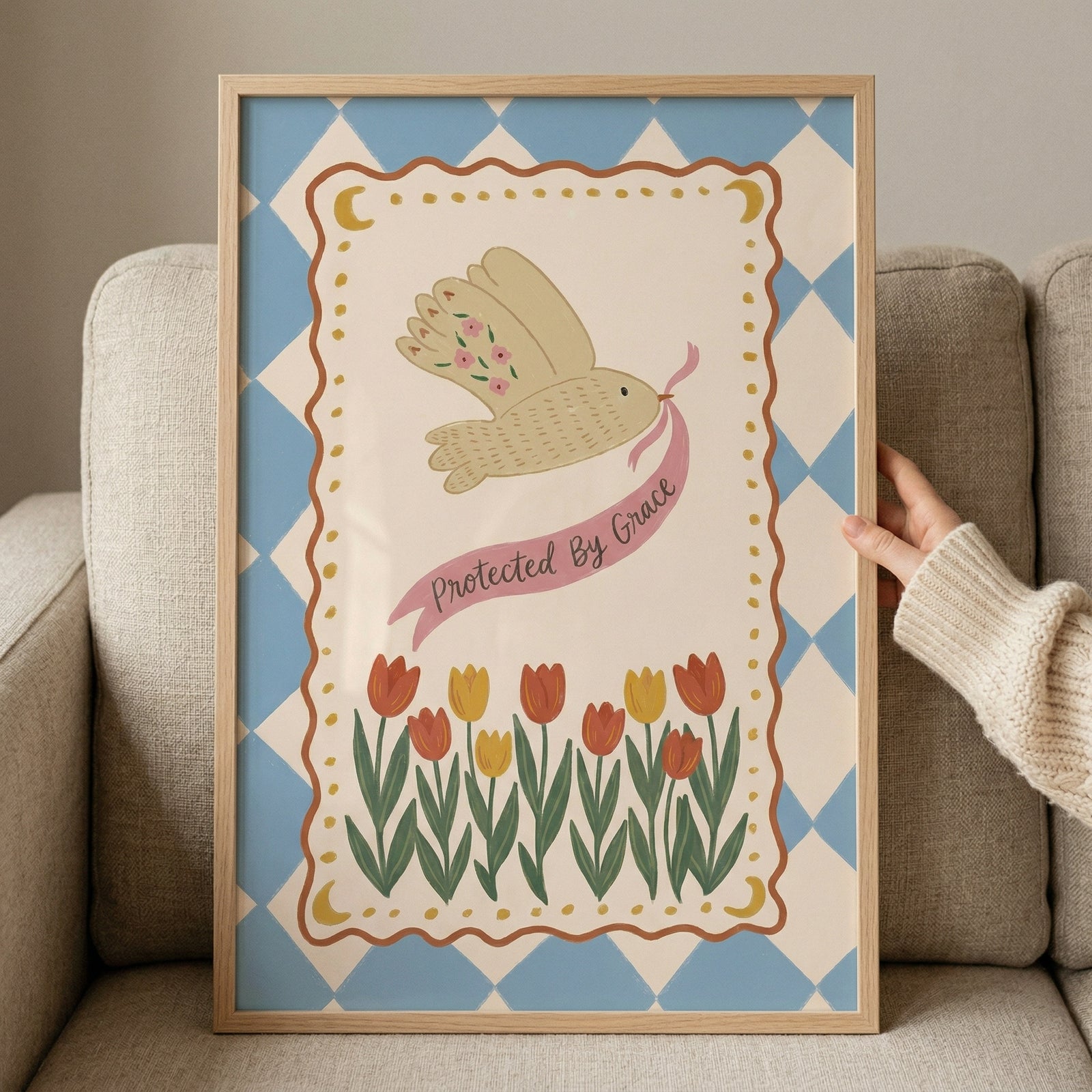 Framed illustration of a bird flying while holding a pink ribbon that reads "Protected By Grace" above a row of red and yellow tulips. The soft blue patterned background and floral details create a gentle and uplifting decorative print.