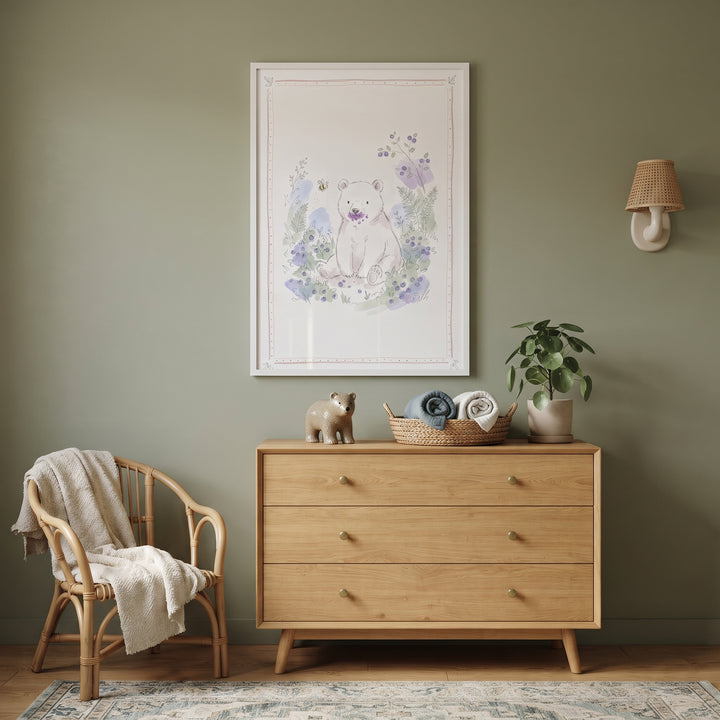 A wood dresser with a plant and basket sits below purple mouth berry bear wall art next to a rattan chair.