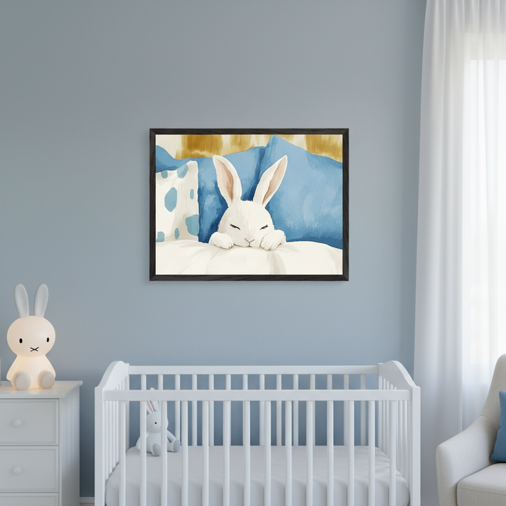Modern nursery with a white crib and dresser against a light blue wall. A framed illustration of a sleeping white rabbit on a white pillow with blue and gold pillows hangs centered above the crib. A Miffy lamp is on the dresser.