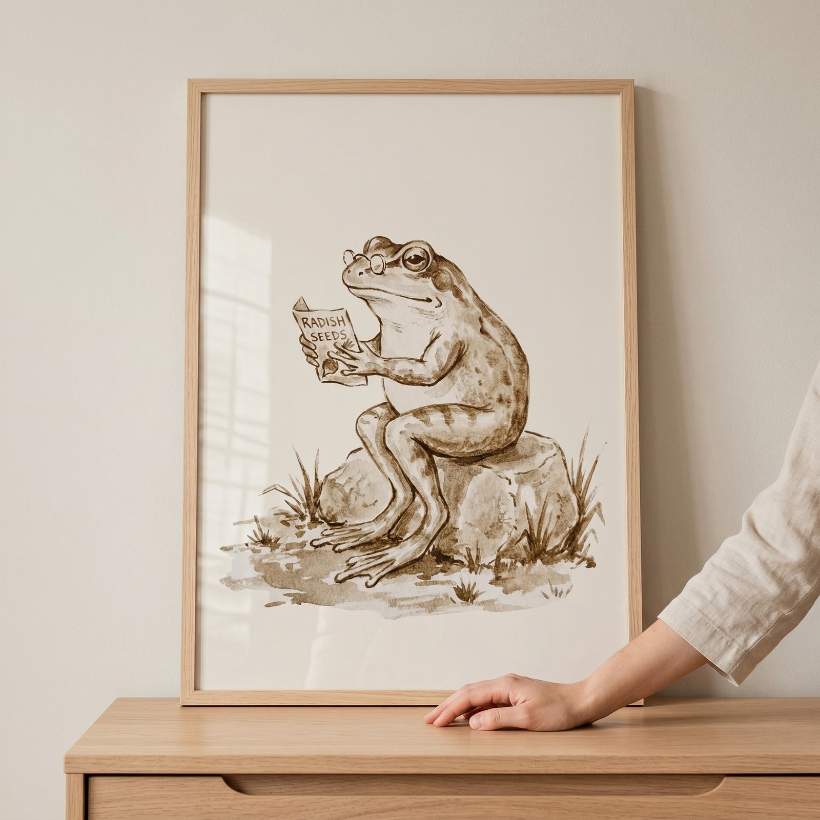 Framed reading radish seeds frog wall art shows a bespectacled frog sitting on a rock and reading a seed packet.