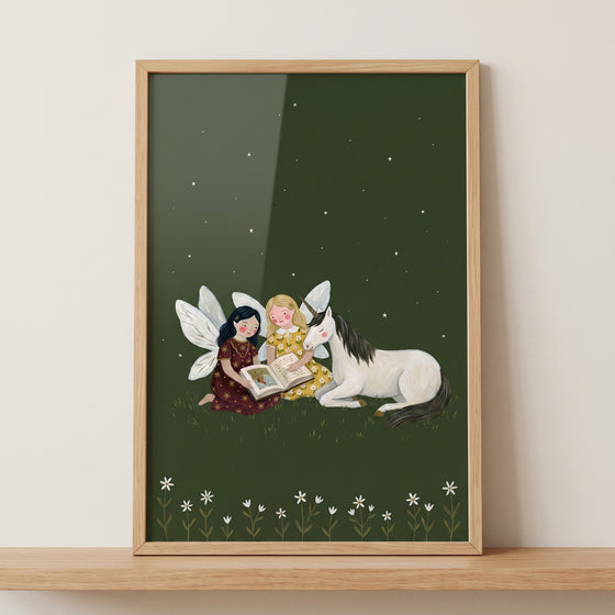Framed reading storybook unicorn fairies wall art with two fairies and a unicorn reading under a starry night sky.