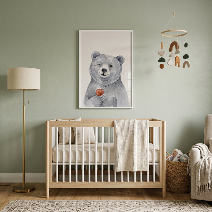 A nursery with a wooden crib, floor lamp, and red apple winking bear artwork on a sage green wall.