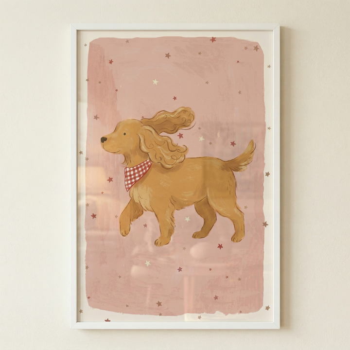 A framed illustration depicts a light brown dog with long, wavy ears and a friendly expression. The animal is shown in a side profile and wears a red and white checkered bandana around its neck. The dog stands against a textured, dusty pink background that features a scattering of small, simple stars in red and white. The entire piece has a soft, whimsical, and hand-drawn quality and is housed in a clean white frame against a neutral-toned wall.