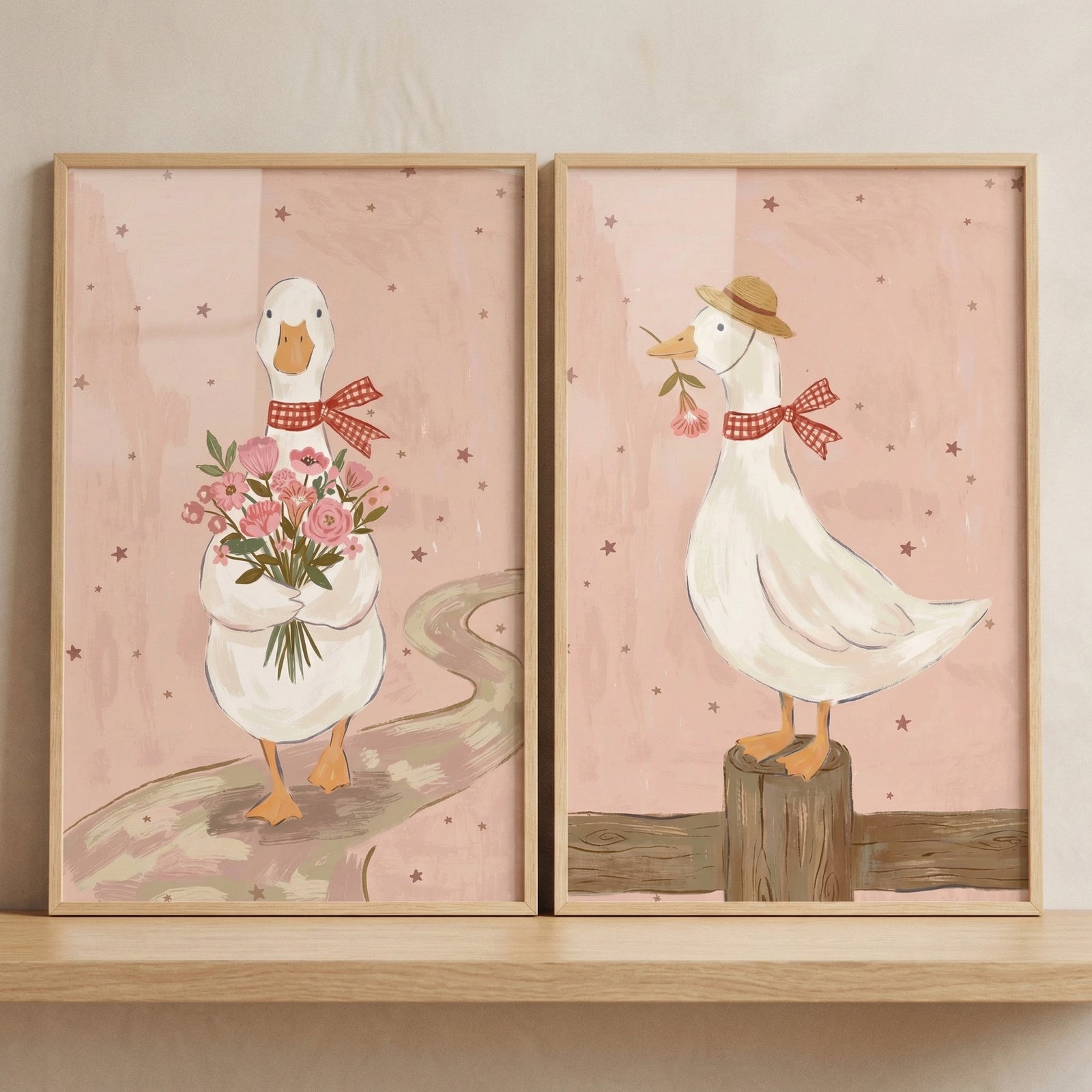 Two framed duck illustrations show a white duck wearing a red gingham bow tie, one holding a bouquet of pink flowers while standing on a winding path and the other wearing a straw hat and standing on a wooden post with a flower in its beak. The soft pink backgrounds and gentle farm style details create a charming and cozy nursery wall art set.