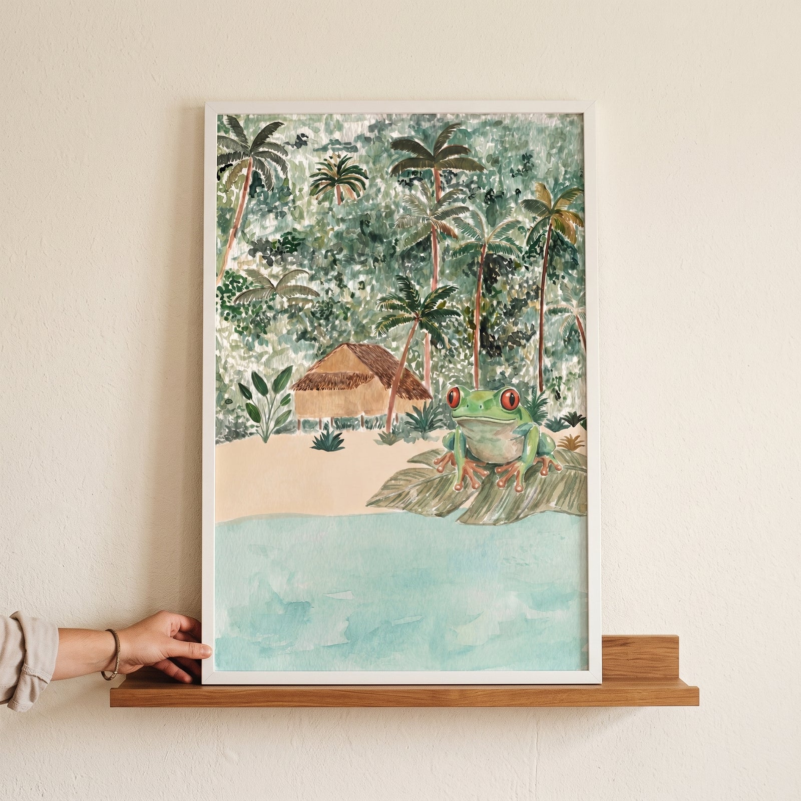 Red eyed tree frog wall art in a white frame on a shelf, featuring a frog on a leaf by a tropical beach and jungle hut.