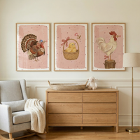 A serene nursery scene features three framed animal illustrations hanging above a light-colored wooden dresser. On the left, a grey rocking chair is draped with a chunky knit throw. The six-drawer dresser holds a woven basket and a small plush sheep. To the right, a simple gold floor lamp stands against the neutral wall. Each framed print showcases a farm animal—a turkey, a chick in a basket, and a rooster on a stump—against a soft pink background with delicate speckles.