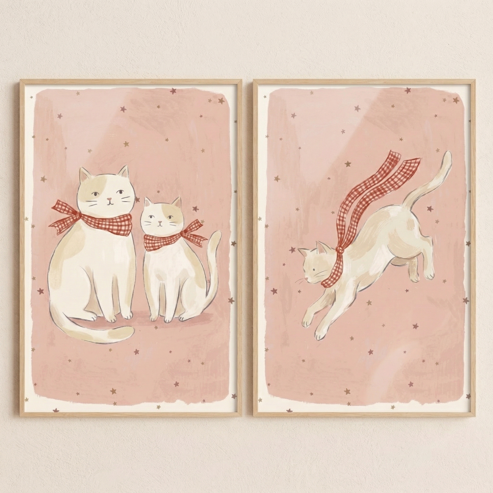 Two vertical wooden-framed pieces of art are displayed side-by-side against a light, textured wall. The illustration on the left shows two cream-colored cats with light brown patches sitting calmly. Each cat wears a red and white checkered scarf tied into a bow. 