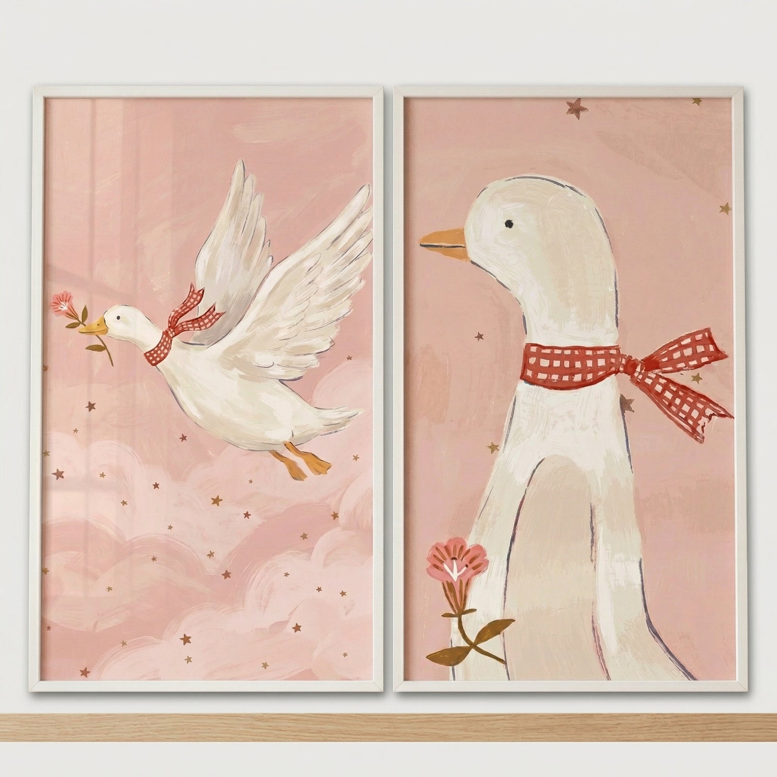 Two framed pastel prints show a white duck wearing a red gingham bow tie, one flying through pink clouds holding a small flower and the other standing calmly with a flower against a soft pink starry background. The artwork adds a whimsical and gentle touch to nursery wall decor with its soft colors and sweet duck illustrations.