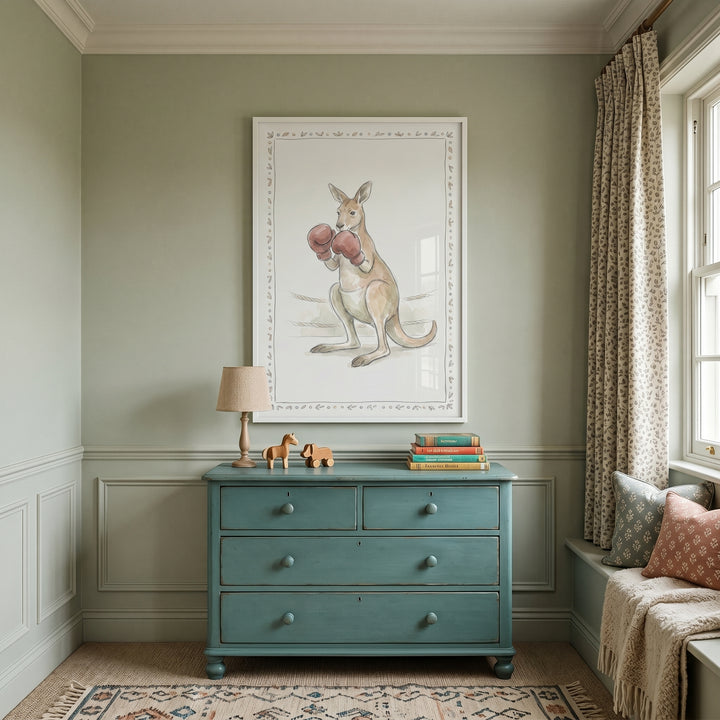 Red glove boxing kangaroo wall art hangs above a teal dresser in a sage room with a window seat and a patterned rug.