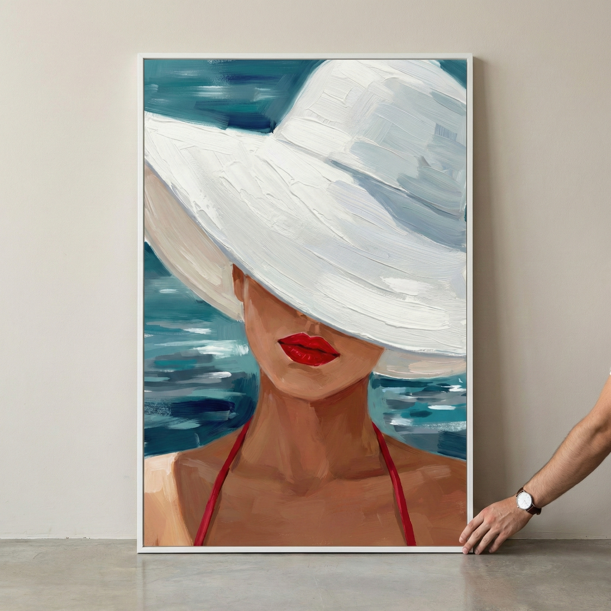 An expressive visual piece captures a woman in a large, wide-brimmed white hat that shields her eyes. Below the brim, vibrant red lips and warm skin are shown. A thin red strap rests on her shoulder. The background is composed of energetic blue and teal horizontal strokes, evoking a water-like setting. The style features thick, layered application, creating a rich texture. This framed image is shown leaning against a neutral wall, with a hand steadying it from the side.