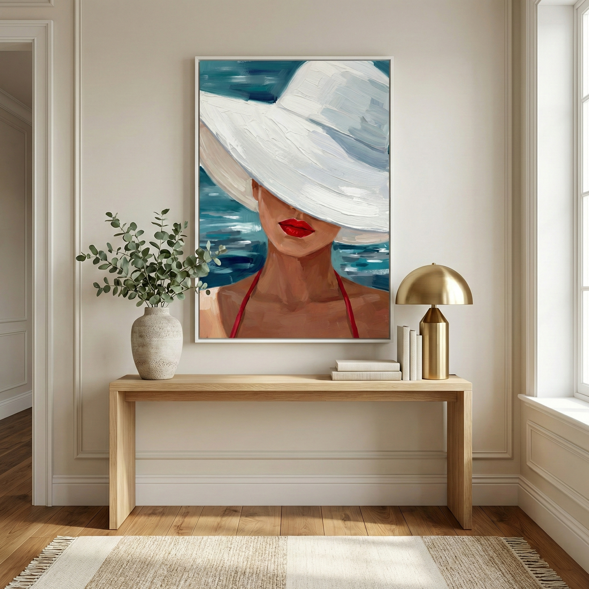 "A large piece of art hangs centered on a neutral-toned wall above a minimalist light-wood console table. The artwork depicts a woman from the shoulders up, her eyes obscured by the wide brim of a large, textured white sun hat. Her lips are a bold, bright red, and she wears a red top with thin straps. Behind her, expressive strokes of blue and teal suggest the surface of a body of water.
