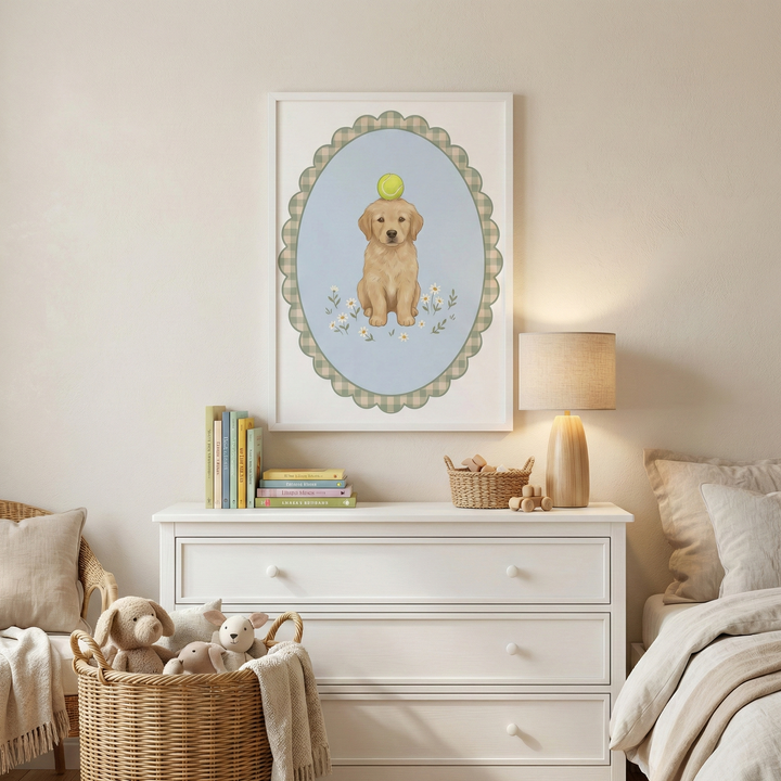 A cozy, soft-toned nursery or child's bedroom. Centered on a cream wall is a white framed illustration of a cute golden-colored puppy sitting and balancing a neon green ball on its head. The puppy is depicted within a scalloped oval frame that has a light blue background and a neutral checkered border, with small white flowers at its feet. Beneath the wall art is a clean white three-drawer dresser. 