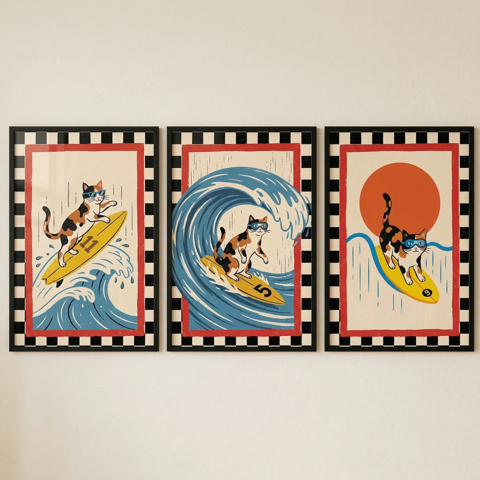 A set of three framed graphic artworks side-by-side on a light-colored wall. Each illustration features a calico cat surfing in a retro, vintage poster style with bold black outlines and a color palette of red, blue, yellow, and cream. The left-most artwork shows the cat wearing blue sunglasses, riding a yellow surfboard numbered ""11"" down a cresting blue wave.
