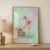 A framed illustration on a wooden surface depicts a whimsical scene. A slender fairy with translucent wings is dressed as a ballerina, wearing a purple bodice and a layered pink tutu. She stands on her toes in ballet shoes, leaning down toward a cluster of mushrooms surrounded by curling green foliage. The background features a soft wash of mint green and lavender. The piece is housed in a light-colored wooden frame, positioned next to a classic lamp with a neutral-toned shade.