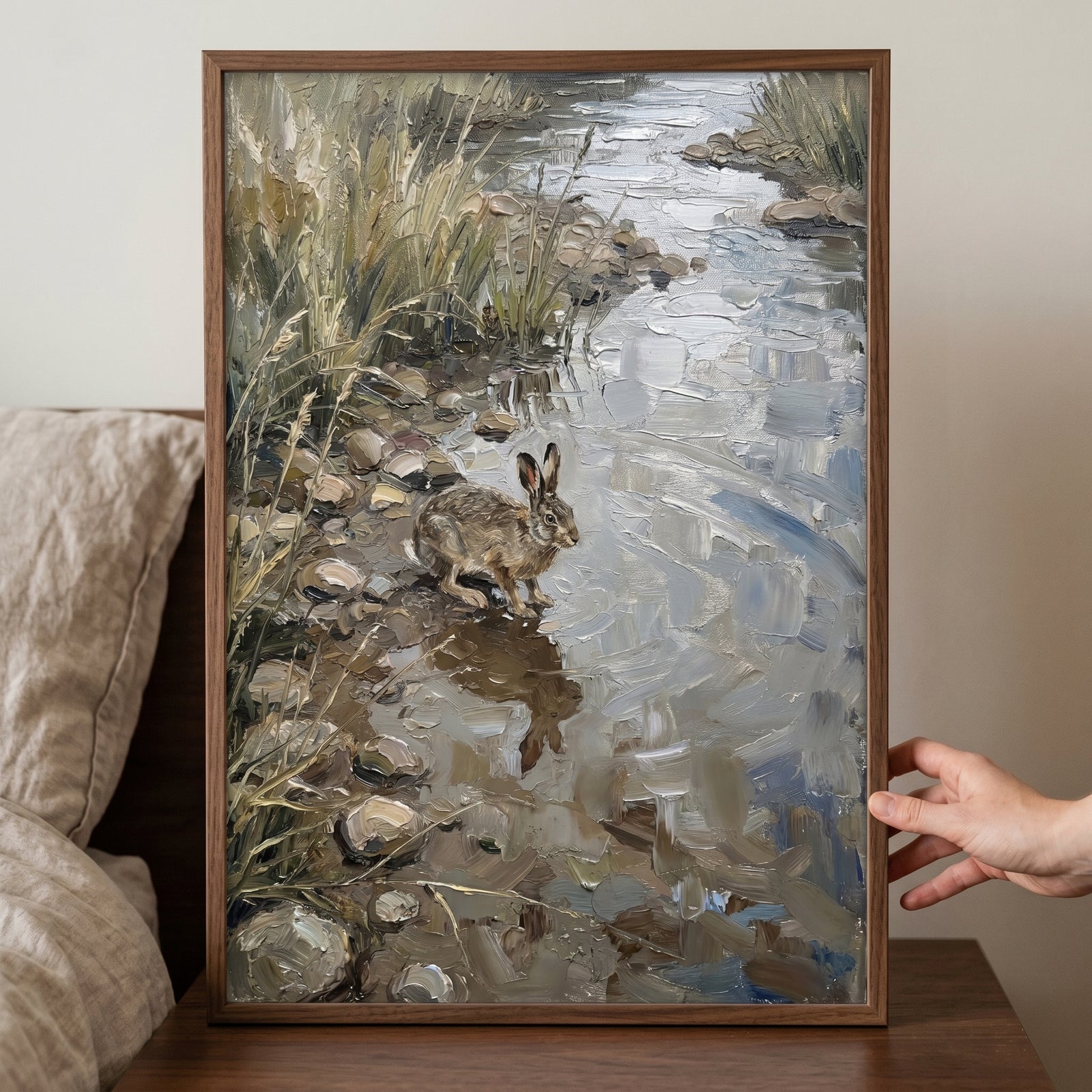 Riverside sitting brown hare wall art in a wooden frame shows a hare by a stream with thick, textured brushstrokes.