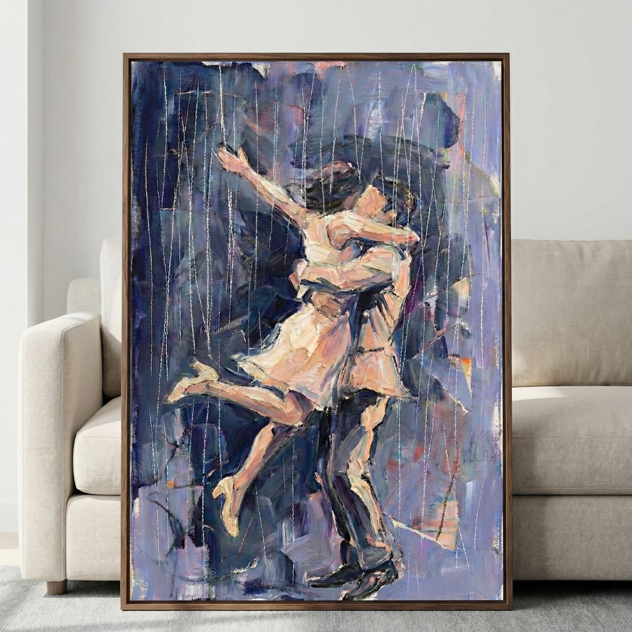 A large framed vertical artwork leans against a neutral-colored sofa. The piece depicts a couple in a passionate embrace during a rain shower. A woman in a light dress and heels is lifted by a man in a light shirt and dark pants. Her leg is kicked back, and an arm is outstretched in joy. The style is expressive with thick, visible brushstrokes and a palette of deep blues, purples, and creams. Thin vertical lines represent falling rain across the textured surface.