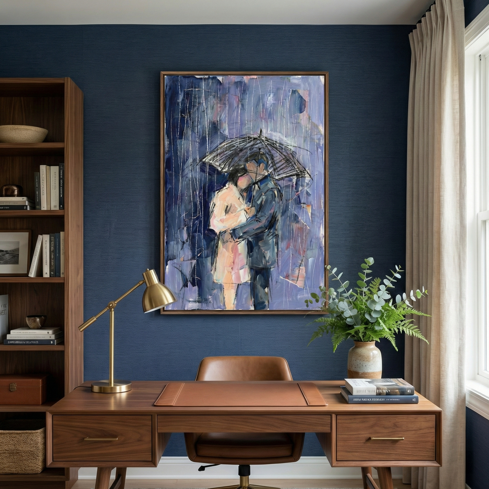 A home office features a dark blue textured wall with a large framed canvas of a couple embracing under an umbrella in the rain. The artwork is done in an expressive style with shades of purple, blue, and pink. Beneath the art sits a wooden desk with a brass lamp, a leather mat, and a vase of eucalyptus. To the left is a tall wooden bookcase filled with various items, and to the right, light-colored curtains hang by a window. A brown leather chair is at the desk.
