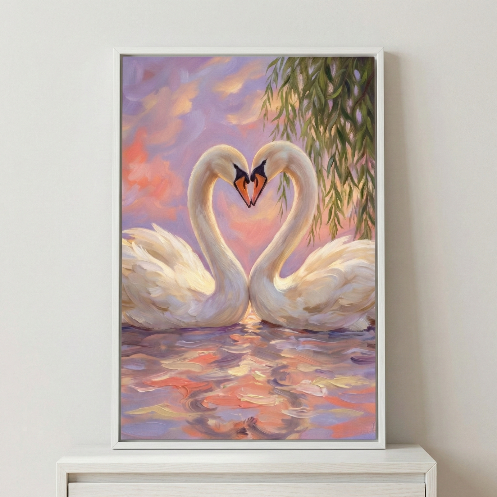 A framed painting of two swans facing each other, forming a heart shape with their necks, set against a vibrant sunset sky with pink and purple hues. Their reflections ripple on the water below, and a willow tree's branches hang gracefully over them.